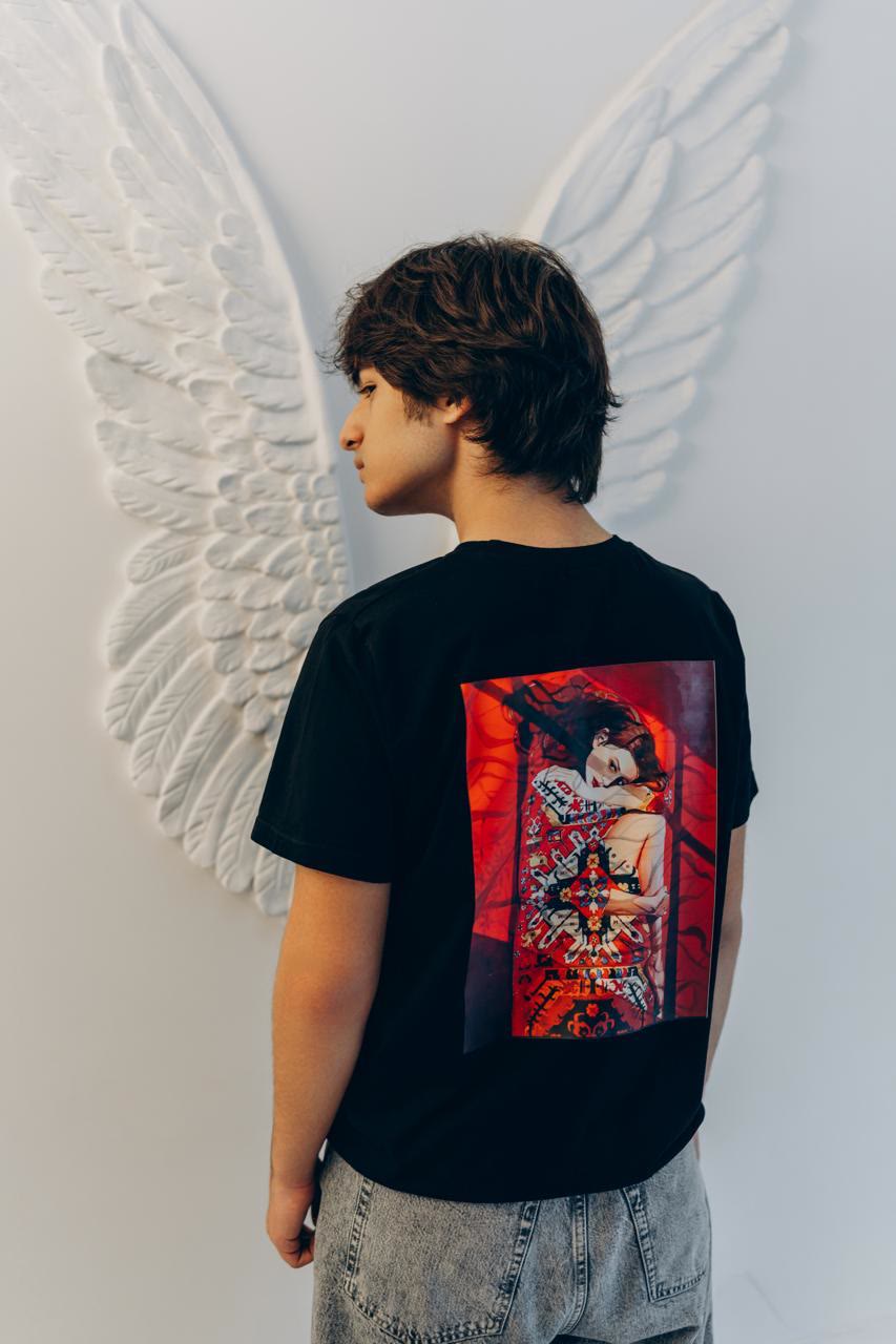 Jamal, seen from behind, in a black T-shirt printed with a painting of a woman wrapped in a red Azerbaijani carpet.