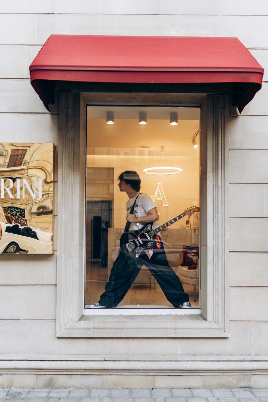 The shop front under a red awning, with Jamal holding an electric guitar in the window.
